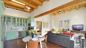 A modern kitchen with green cabinets, a dining table with chairs, and a gray sofa in a living area with a TV and decorative items. - 3 Bedroom, 3 Bath Home plus 1 Bedroom, 1 Bath Casita -12 min. to Santa Fe center (Santa Fe)