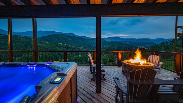 Un jacuzzi con panel digital, un brasero y mobiliario exterior en una terraza de madera con vistas panorámicas a la montaña.