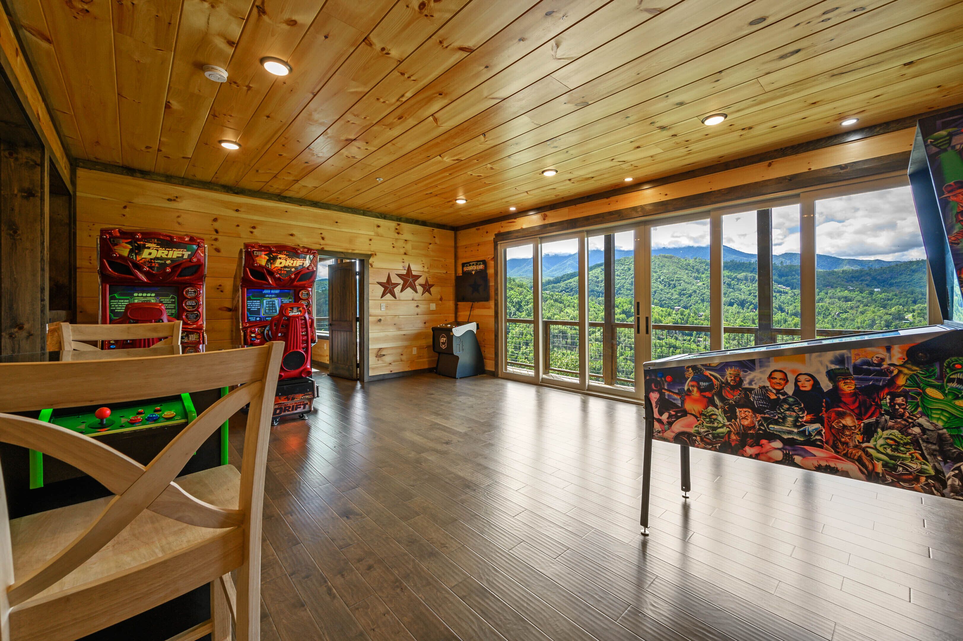 Interior de madeira com jogos de fliperama, uma grande janela com vista para as montanhas e um mural.