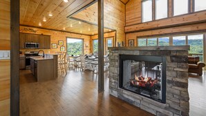 Un interior de cabaña espacioso con chimenea de piedra, pisos de madera y ventanas amplias que dan vista al bosque.