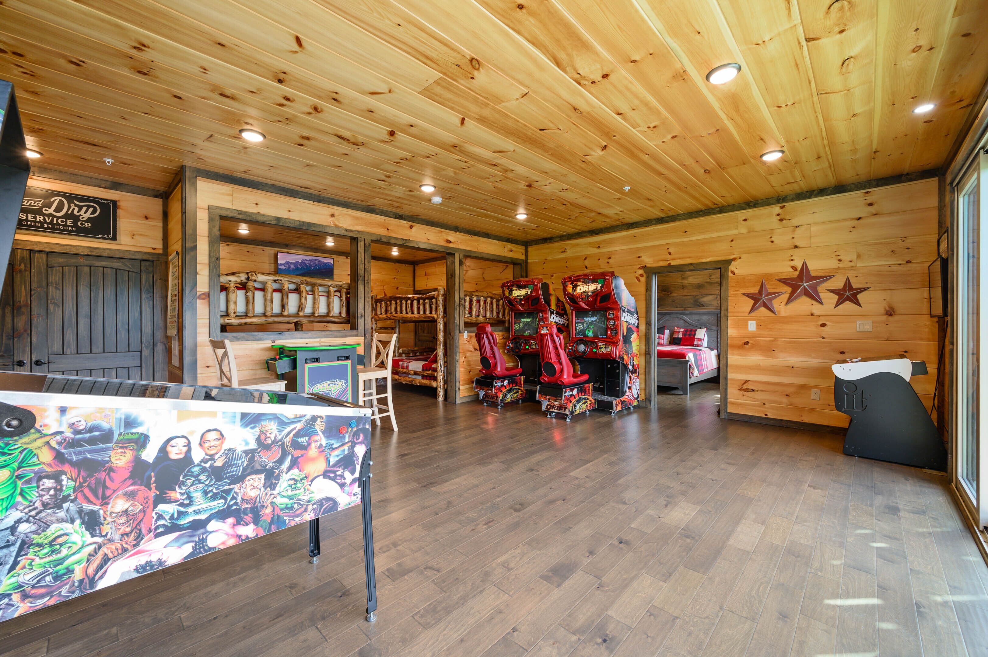 A room with wooden walls and ceiling, a mural on the left, and arcade games in the center.