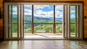 Habitación con grandes puertas correderas de vidrio que dan a una terraza con vista a la montaña.