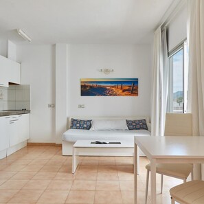 Un espace de vie moderne et minimaliste comprenant un coin cuisine, un canapé agrémenté de coussins à motifs et une table à manger.