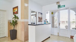 A reception area with a reception desk, a potted plant, and a painting on the wall. - Apartamentos San Antonio Beach (Sant Josep de sa Talaia)