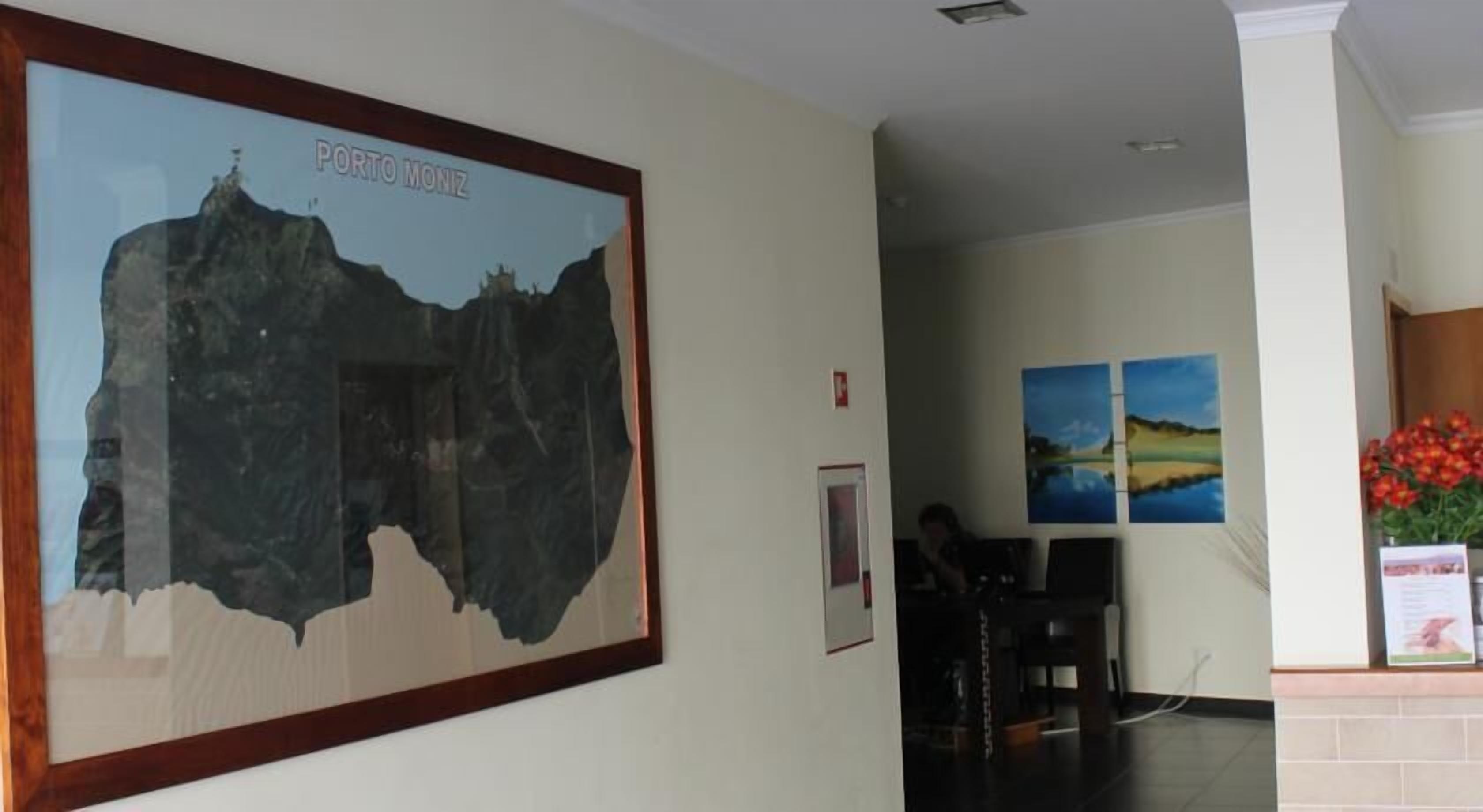 A framed map of Porto Moniz, a reception area with a desk, chairs, and two landscape paintings on the wall.