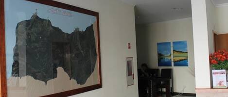 A framed map of Porto Moniz, a reception area with a desk, chairs, and two landscape paintings on the wall.