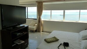 A hotel room with a large TV, a bed, a chair, and a window with a view of the sea. - Penthouse Sun Rise San Andrés (San Andrés)