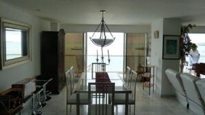 A dining area with a glass table and chairs, a chandelier, and a view of the sea through a large window. - Penthouse Sun Rise San Andrés (San Andrés)