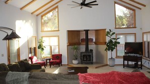 Un vaste salon doté d’un haut plafond, de grandes fenêtres, d’une cheminée, d’un téléviseur et d’un coin salon confortable avec un canapé et des fauteuils.