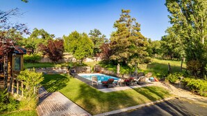 Un jardin avec une piscine, une terrasse en bois et un espace closPlanté d'arbres.