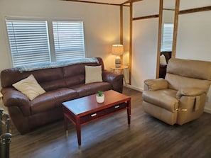 A living room with a brown leather sofa, a wooden coffee table, and a beige recliner.
