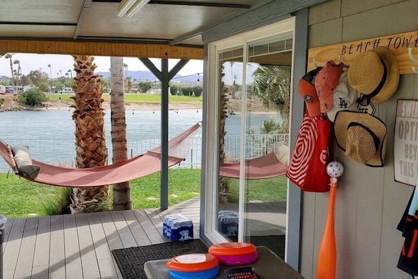 A covered outdoor area with a hammock, palm trees, and a view of a lake.