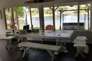 A dining area with a long table and benches, large windows with a view of a lake and trees, and a covered outdoor seating area.