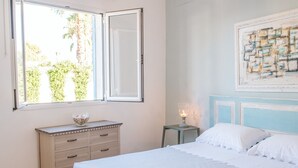 Un dormitorio con cama, cómoda, mesita de noche, ventana y un cuadro en la pared.