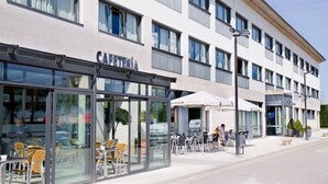 Moderni hotelli, jossa on lasijulkisivu, ulkotila istumiseen ja esteetön näkymä kadulle.