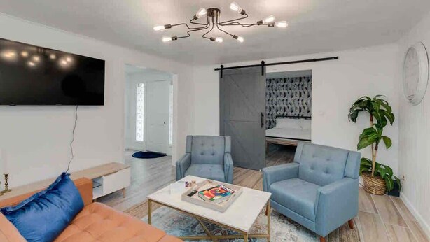 A modern living room with a sofa, two armchairs, a coffee table, and a TV mounted on the wall. - Cozy Alice at Central: 3BR + Fenced Yard (Phoenix)