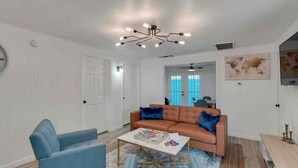 A living room with a blue sofa, a coffee table, and a unique chandelier. - Cozy Alice at Central: 3BR + Fenced Yard (Phoenix)