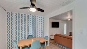 A modern living room with a wooden dining table, teal chairs, a ceiling fan, and a patterned wall. - Cozy Alice at Central: 3BR + Fenced Yard (Phoenix)