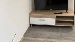 Una sala de estar moderna con un televisor de pantalla plana sobre un mueble de madera, un control remoto y un cajón pequeño.