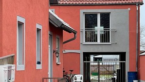 Un edificio rojo con tejado de tejas, entrada protegida por una verja y patio empedrado.