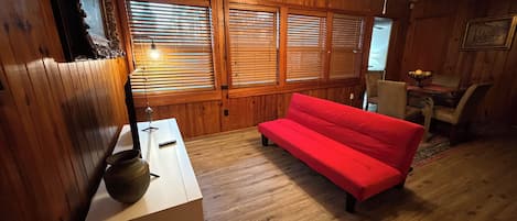 A room with a wooden floor, a red sofa, a white table with a vase, and a ceiling fan.