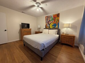 A bedroom with a bed, a television on a wooden dresser, a ceiling fan, and a painting on the wall. - Private 3BR Home • 4 Queen Beds + 3 Sofa Beds • Great Location (Valdosta)