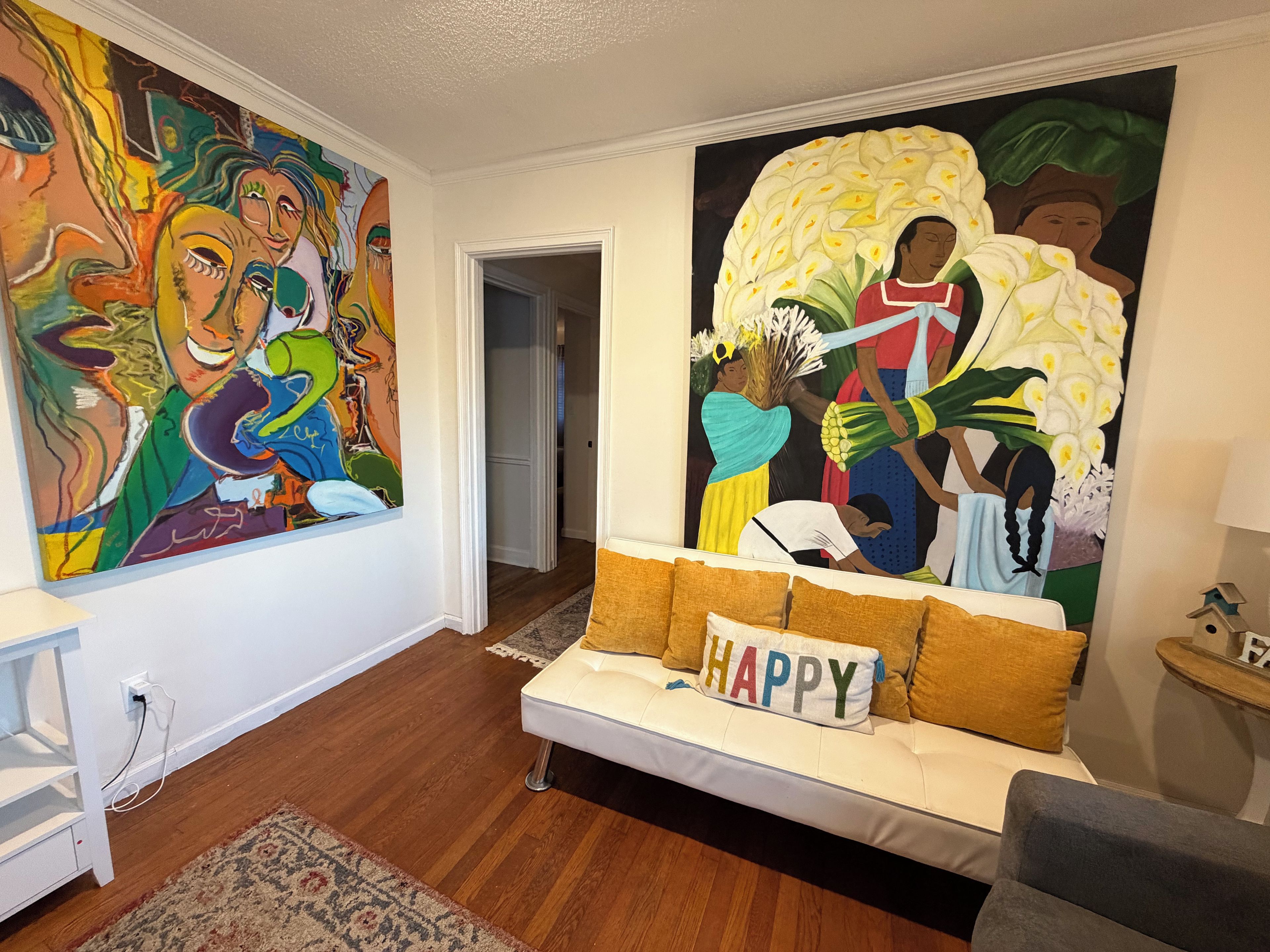 Uma sala de estar com um sofá branco, uma pintura abstrata colorida na parede e um grande mural retratando pessoas e flores.