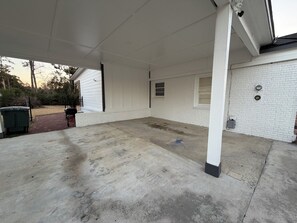 A covered outdoor area with a concrete floor, a brick pathway, and a white brick wall.