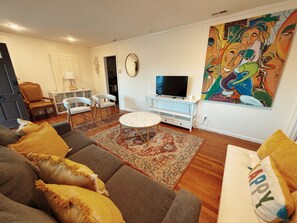 Una sala de estar con un sofá, sillas, una mesa de centro, un televisor y un cuadro en la pared.