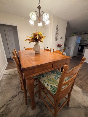 Un comedor con mesa de madera, sillas, un jarrón con flores y una araña.
