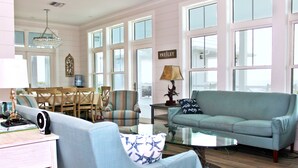 A spacious living room with a light blue sofa, a glass coffee table, and a dining area with a wooden table and chairs.