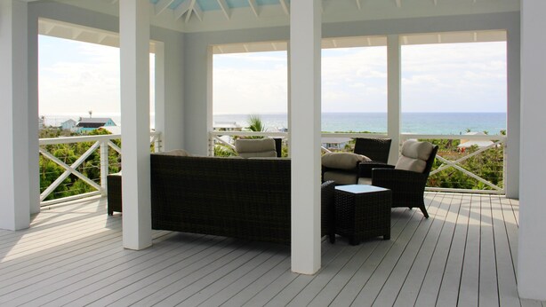 A covered outdoor seating area with wicker furniture and a view of the ocean.