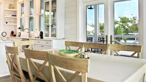 A modern kitchen with white cabinetry, a dining table with wooden chairs, and large windows offering a view of the outdoors.