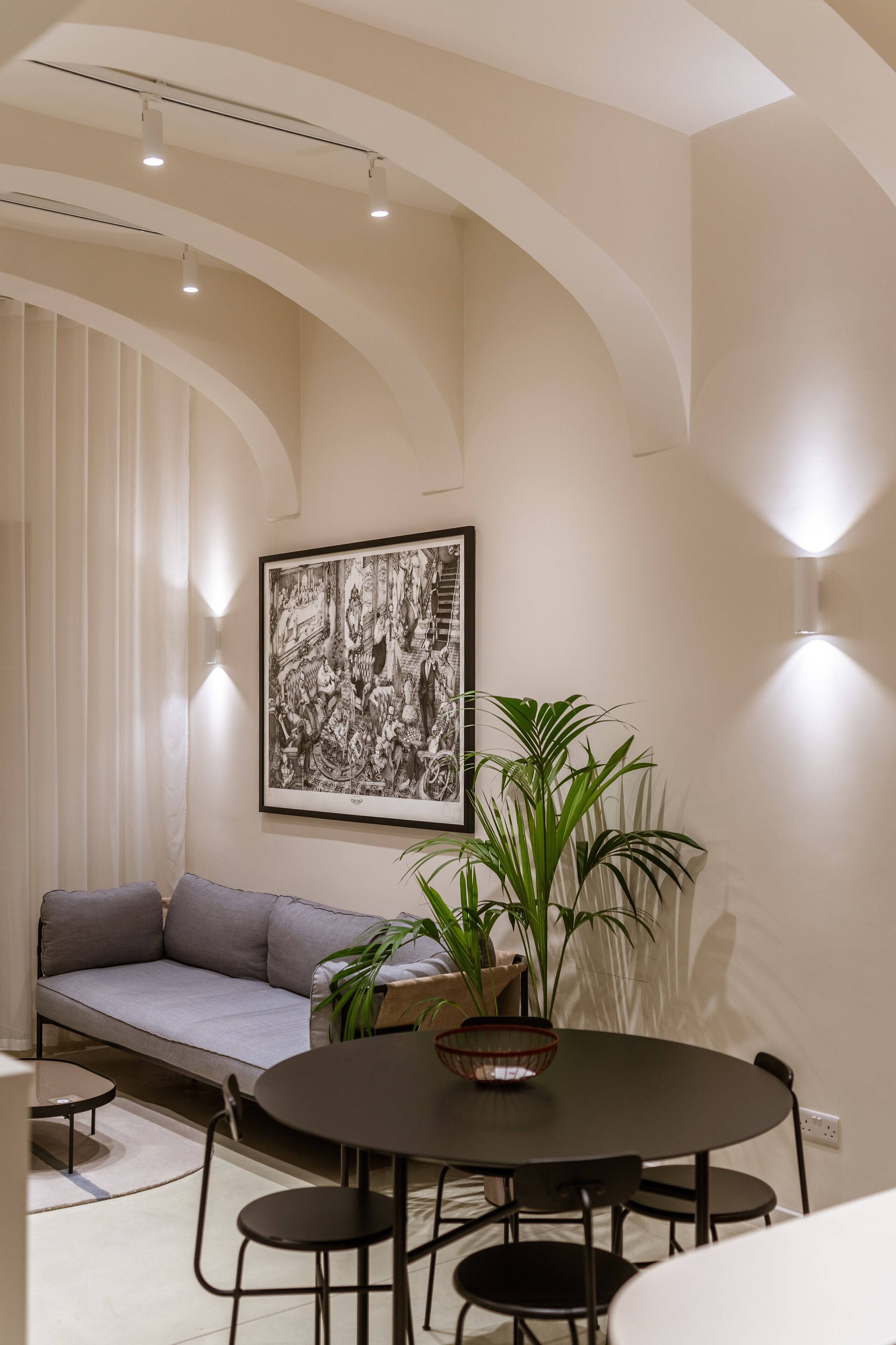 Un comedor moderno con una mesa redonda, cuatro sillas, un sofá gris y una obra de arte grande con marco en la pared.