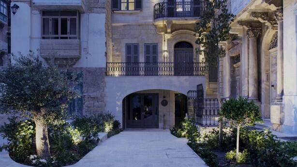 Un immeuble à plusieurs étages doté d’une entrée centrale, de balcons et d’une cour intérieure avec des arbres.