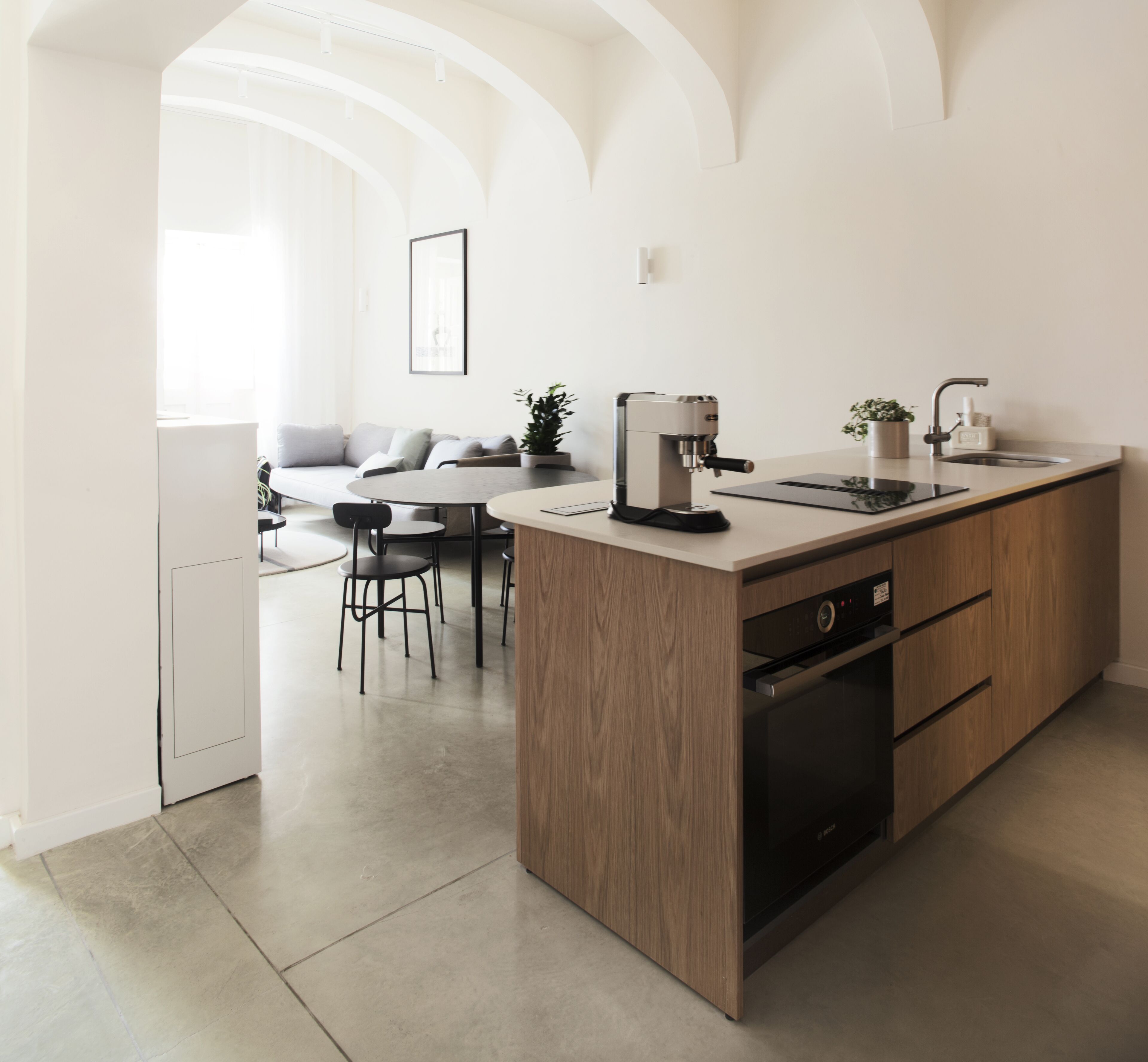 A modern kitchen with a built-in dishwasher, a coffee machine, and a sink. There is a dining area with a table and chairs.