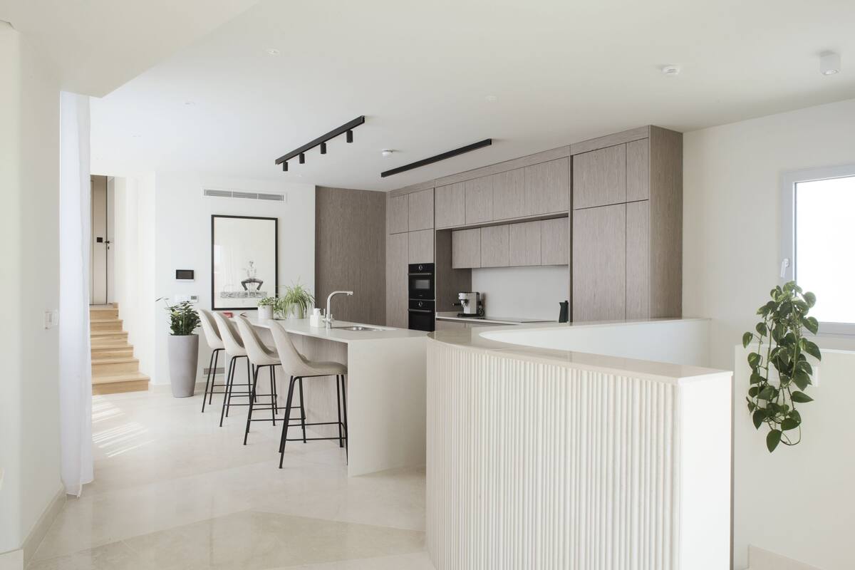 Una cocina moderna con una isla central, taburetes de bar y una escalera que conduce a un nivel superior.