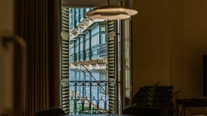 Un coin repas comprenant une table et des chaises, un luminaire suspendu et une vue sur un bâtiment par une fenêtre.