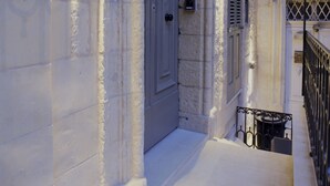 Une ruelle étroite bordée d’un bâtiment en pierre, avec une porte fermée et un petit balcon doté d’une rambarde en métal.