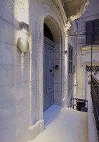 A narrow alleyway with a stone building, a closed door, and a small balcony with a metal railing.