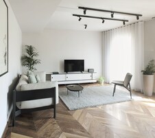 Una sala de estar moderna con un sofá, un televisor sobre un mueble blanco, una mesa de centro y una silla.