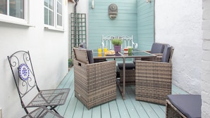 Une terrasse avec des meubles en osier, une table agrémentée d’une plante en pot et une porte bleue.