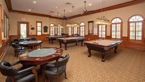 A billiards room with multiple tables and chairs, wooden paneling, and large windows. - Spacious 2BR Villa | Pools | Near Beach & Dining | Garage Parking (Port Orange)