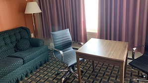 A hotel room with a green patterned sofa, a blue chair, a wooden table, and a floor lamp. - Ashland Motel (Ashland)