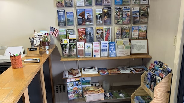 A reception desk with a wooden counter, a small American flag, and a 'Thank You' sign. Behind the desk, there are shelves with various travel brochures and maps. - Ashland Motel (Ashland)