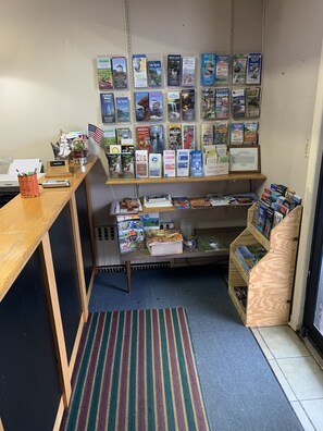 A reception desk with a wooden counter, a small American flag, and a 'Thank You' sign. Behind the desk, there are shelves with various travel brochures and maps.