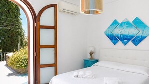 Ein Hotelzimmer mit Bett, Nachttisch, Wand-Klimaanlage, Fenster mit Blick auf Grünflächen und einer Deckenleuchte.