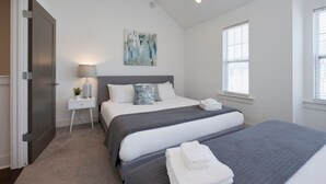 Ein Schlafzimmer mit einem großen Bett, einem Nachttisch mit Lampe und einem Fenster mit Jalousien.