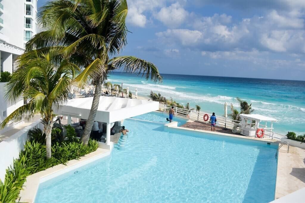 A pool with a view of the ocean, palm trees, and a lifeguard stand.