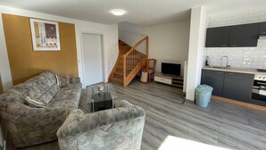 Un espacio habitable compacto con sofá, un televisor pequeño, una zona de cocina y una escalera.